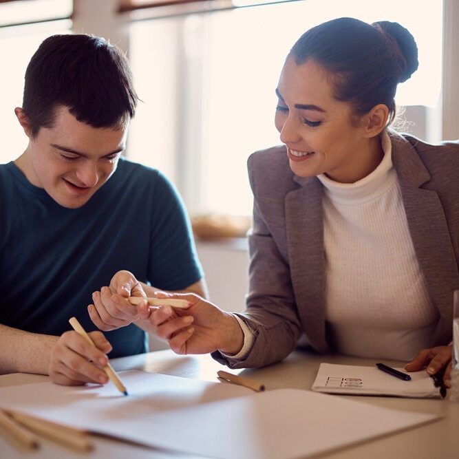 Happy down syndrome man and his psychologist drawing together on the paper during home visit.