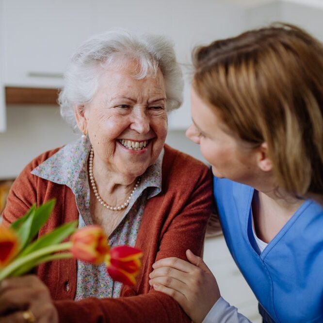 Senior woman and nurse with tulip bouquet.